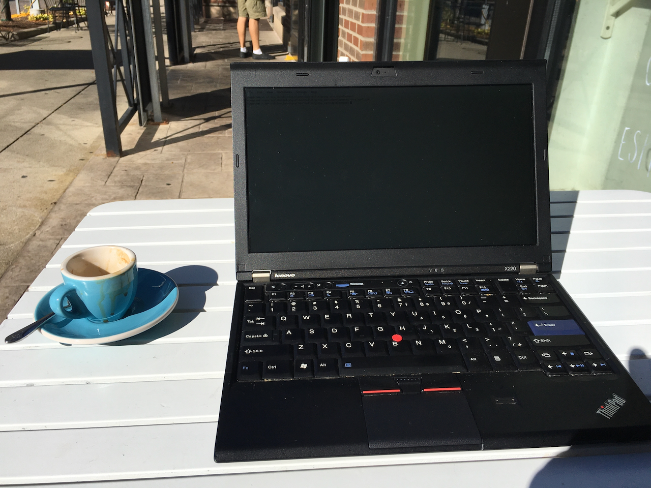 A Thinkpad X220 laptop on a table with an espresso next to it outside on a city street
